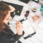 Jeune épargnante réfléchissant à ses choix d'investissement, carnet et ordinateur sur un bureau
