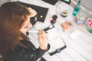 Jeune épargnante réfléchissant à ses choix d'investissement, carnet et ordinateur sur un bureau