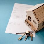Maquette de maison en bois posée sur un document avec un trousseau de clés, symbole de la fiscalité de la propriété