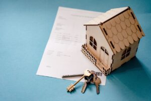Maquette de maison en bois posée sur un document avec un trousseau de clés, symbole de la fiscalité de la propriété