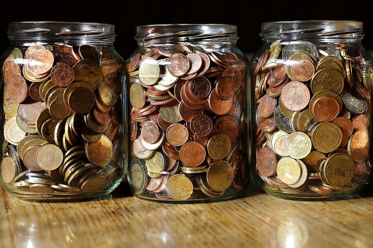 Trois bocaux remplis de pièces en euros alignés sur une table en bois